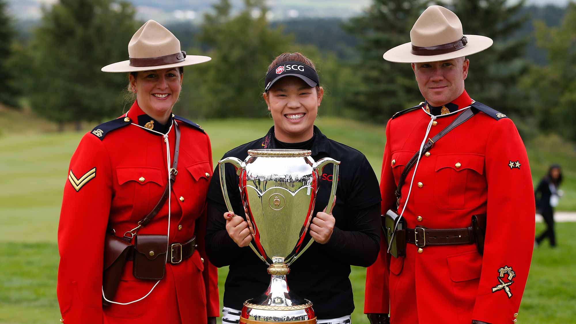Ariya Jutanugarn of Thailand holds the Canadian Pacific Women's Open trophy with two members of there Canadian Royal Mounted Police after she won the event at Priddis Greens Golf and Country Club