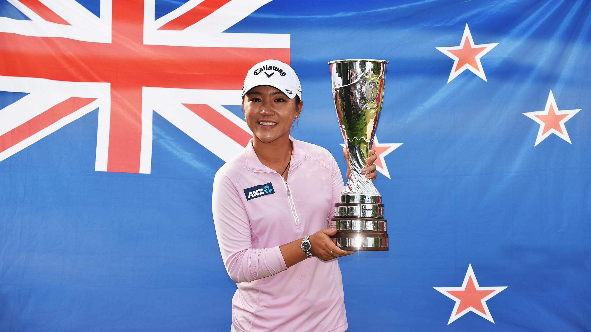Lydia Ko posing with the Evian Championship Trophy in front of the official flag of New Zealand