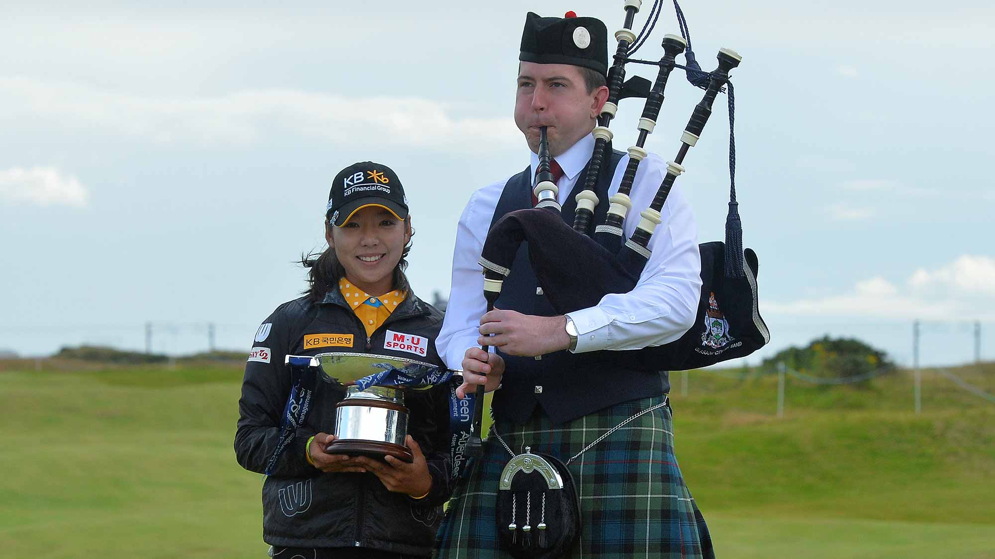 Mi Hyang Lee of Korea winner of the Aberdeen Asset Management Ladies Scottish Open poses for a photograph with a bag piper on the 18th green after the final round at Dundonald Links Golf Course